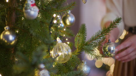 close-up of woman's hand putting bauble on christmas tree