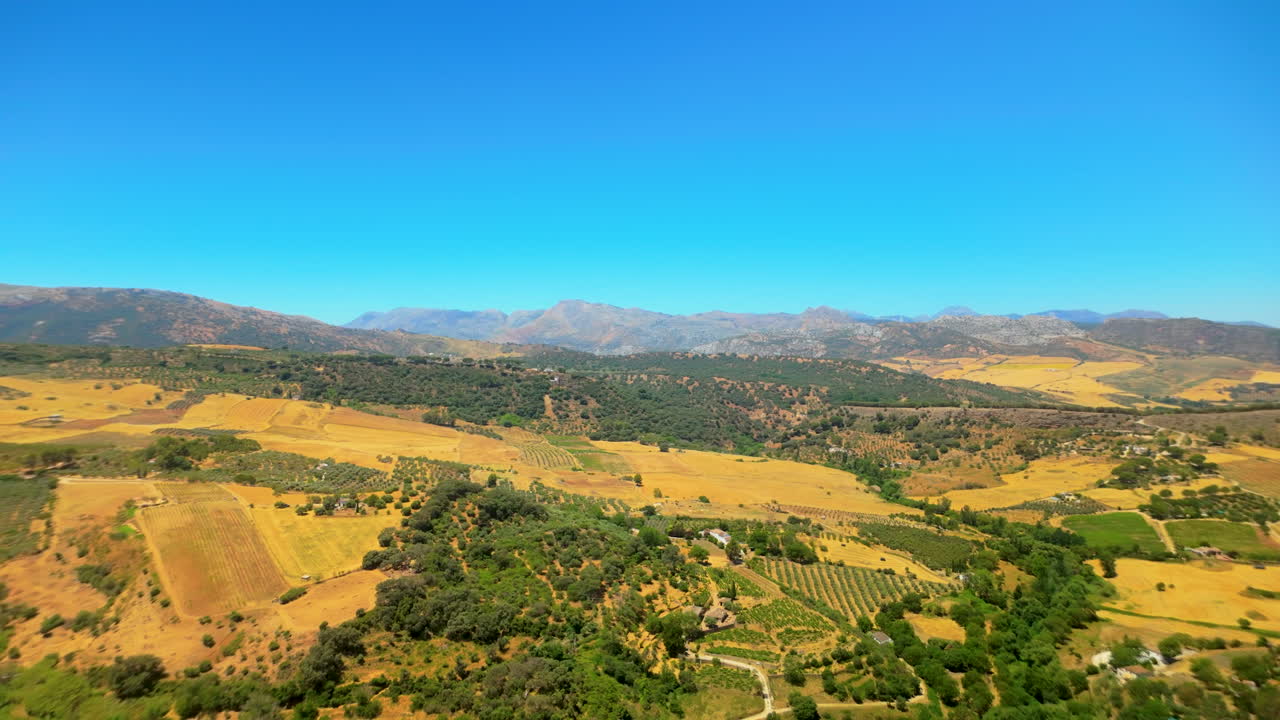 vista aérea expansiva de colinas onduladas y campos agrícolas con una cordillera en el fondo bajo un cielo azul claro