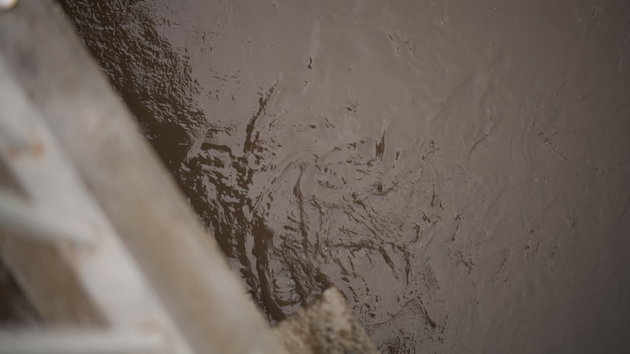 Acqua urbana fangosa con riflessi. Pozzanghera urbana intrisa di pioggia che riflette il cielo cupo sopra una struttura. Superficie fangosa e luccicante di una pozzanghera piena di pioggia con increspature e riflessi della città sull'acqua.