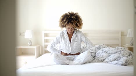 chica con dolor de estómago sentada en la cama