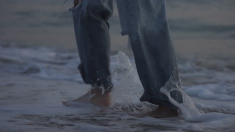 girl walking barefoot in long jeans along the shore of the beach during sunset