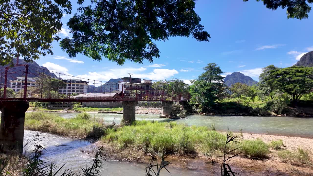 Nam Song Motorcycle Bridge spans river with lush greenery and mountain backdrop in Laos