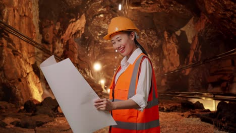 side view of asian female engineer with safety helmet looking at blueprint in her hands in underground mine tunnel