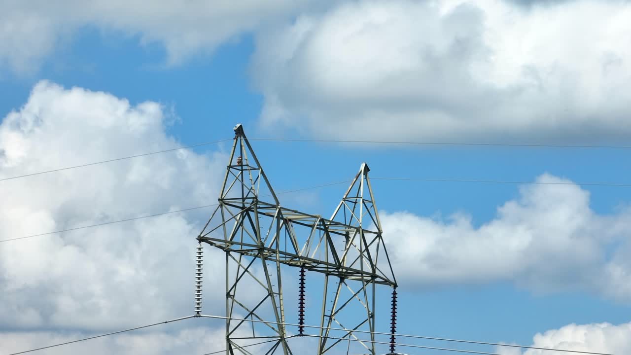 Electric power lines against blue sky with white puffy clouds
