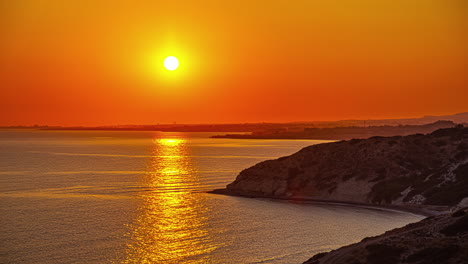 time lapse shot of an orange sunset at aphrodite's rock on the island of cyprus