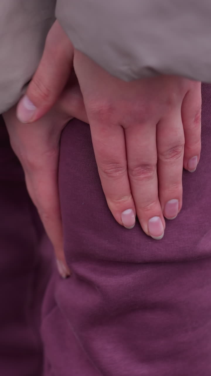 primer plano de una persona con traje de invierno frotando la rodilla izquierda, posiblemente con dolor, manos presionando sobre pantalones marrón con tensión visible, fondo nevado borroso