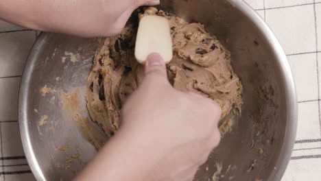 person mixing cookie dough using spatula on stainless bowl