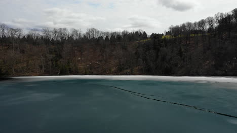 Drone-flying-down-and-into-forest-at-a-blue-icy-lake-green-lake-new-york-state-park