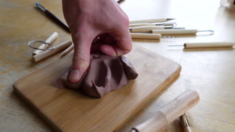 An-artist-sculpting-a-project-with-soft,-brown-modeling-clay-using-his-hands-and-fingers-to-shape-and-mold-the-project-on-a-messy-art-studio-table-with-tools