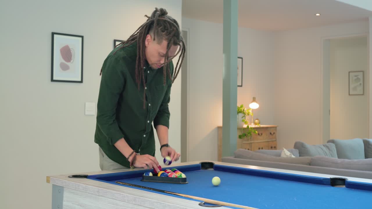 Man is approaching blue-felt pool table, lifting black rack and arranging balls for break shot