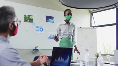 african american woman wearing face mask giving presentation to her colleagues at modern office