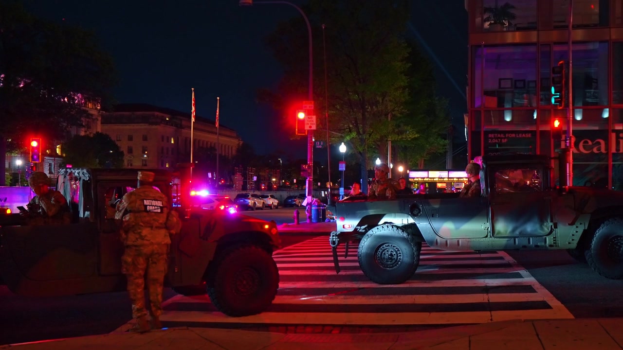 Washington, USA, 1 Jule 2026 : National guard military vehicles and soldiers at city intersection at night. Camouflage trucks and uniformed personnel stopped at red light crosswalk on street.