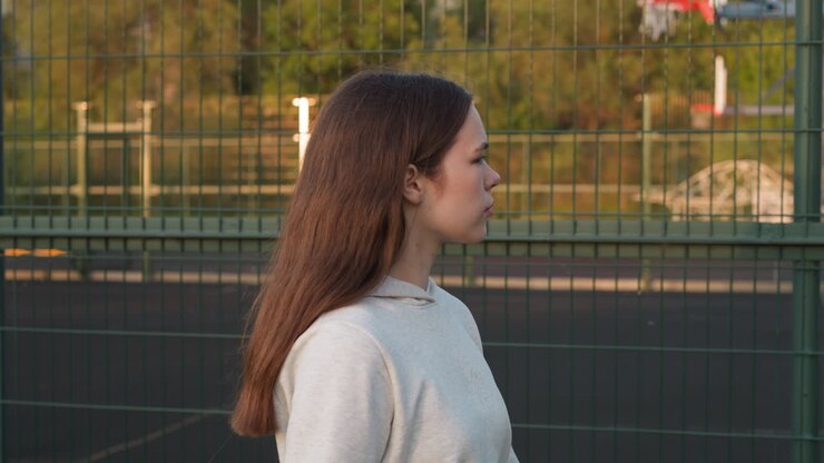 Lady passes by fence of stadium alone at sunset. Young woman sadly looks at sports field thinking about fear of failure. Fighting inner worries