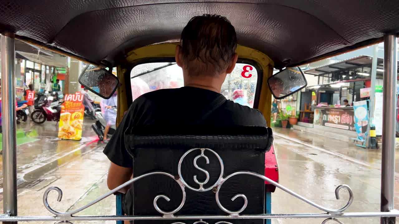 Passenger’s rear view inside tuk-tuk navigating wet Bangkok streets, passing motorcycles and cars in daylight with overcast, diffused lighting and steady camera