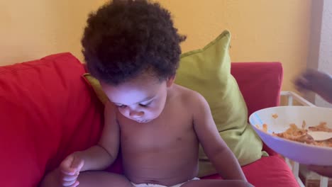 african european exotic two year old child eating nigerian typical food by himself seated in the sofa