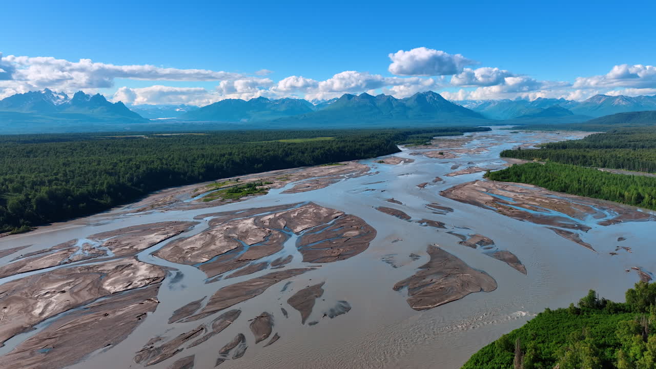 Sorvolo dello straordinario paesaggio naturale dell'Alaska, USA. Filmato aereo con drone sull'ampio delta del fiume poco profondo e ramificato che scorre nelle lussureggianti foreste. Montagne spettacolari sullo sfondo.