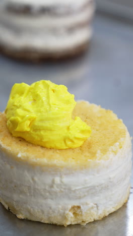 little vanilla sponge cake is covered with bright yellow butter cream. desserts decoration at modern food factory. close up. vertical video