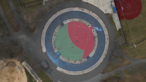 a top down view directly above a circular track and sports field in an empty park on a cloudy afternoon