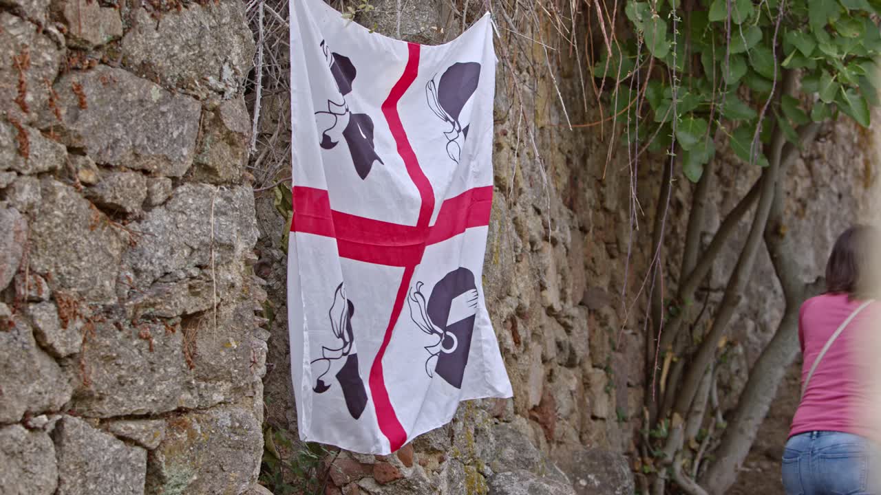 Beautiful white and red flag of Sardinia waving on side of stone wall, close up view