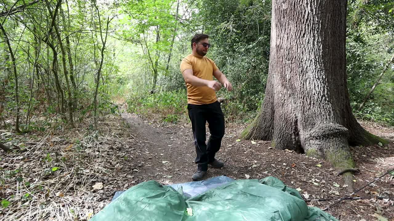 Angry man who fails to assemble a camping tent and throws it on the ground at a campsite in the forest