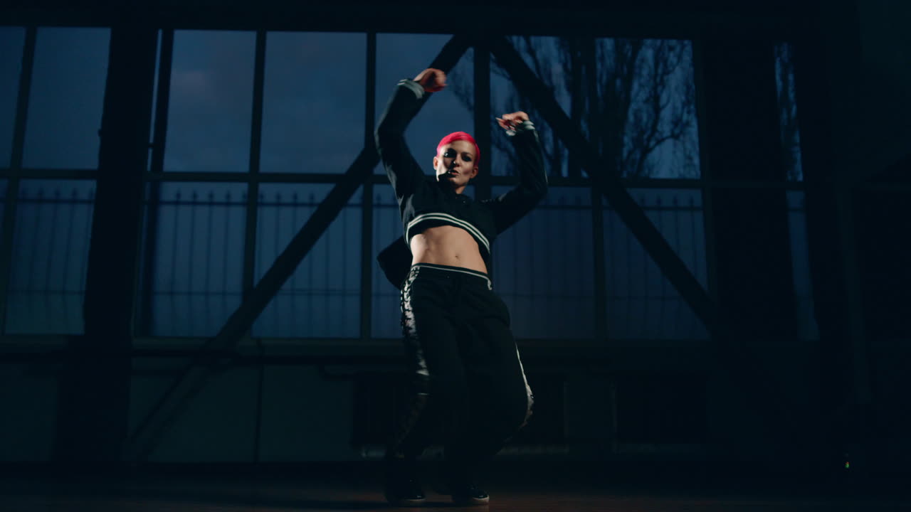 Sporty woman dancing hip hop in dark class. Female dancer practicing in studio.