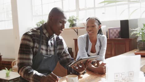 Happy-african-american-female-and-male-coffee-shop-owners-talking-and-using-tablet,-slow-motion