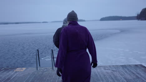 A-couple-in-their-50s-approach-the-icy-lake,-the-man-climbs-in