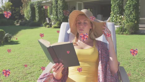 animation of floral hearts falling over cauacsian woman in sun lounger reading book in garden