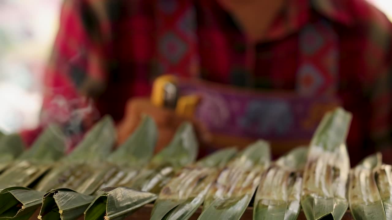 persona asando bocadillos envueltos en hojas de plátano