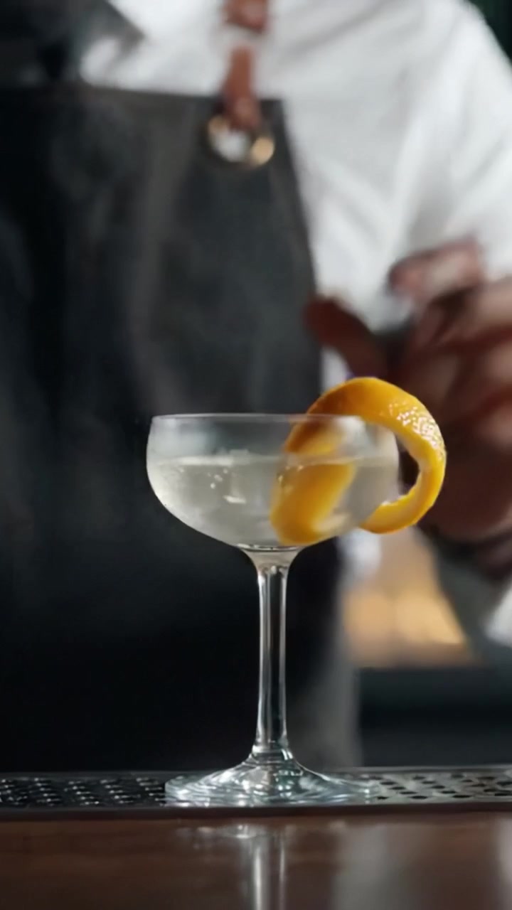 Creazione di un Cocktail d'Autore: Il Barista Taglia una Scorza d'Arancia per il Tocco Finale Perfetto su un Bicchiere di Martini Ghiacciato