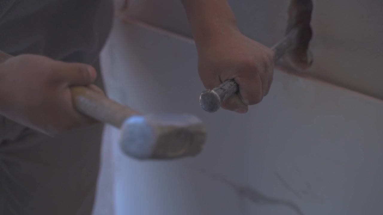A closeup shot of handheld chiseling the wall with a steel chisel and a club hammer.