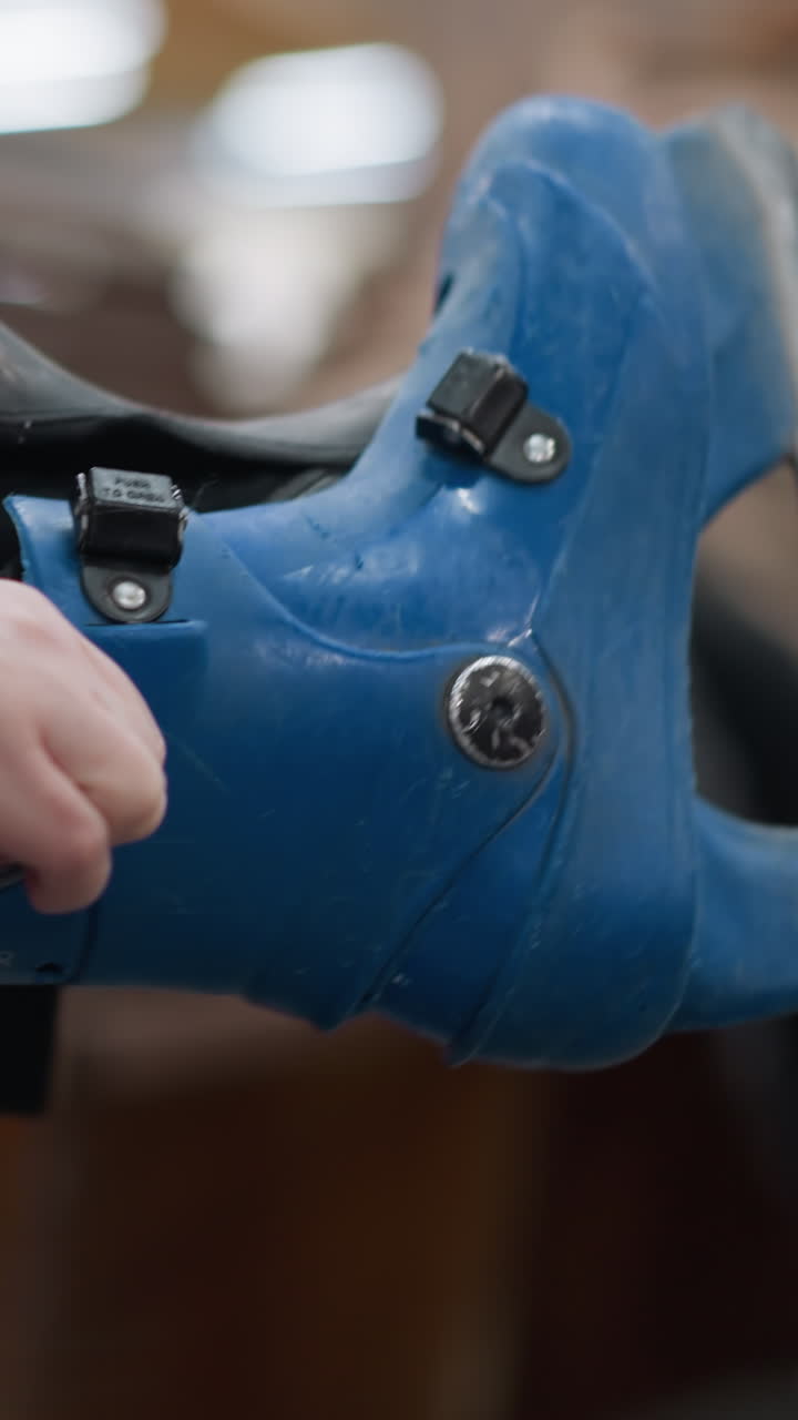 primer plano de una persona que lleva patines de hielo azules mientras los ajusta, con un enfoque en las manos y los pantalones negros, con un fondo borroso