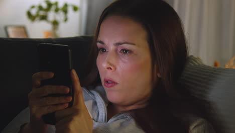 Close-Up-Of-Woman-Lying-On-Sofa-At-Home-At-Night-Streaming-Or-Looking-At-Online-Content-On-Mobile-Phone