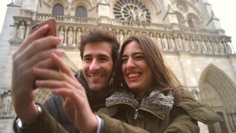 una pareja tomando una selfie frente a la catedral de notre dame