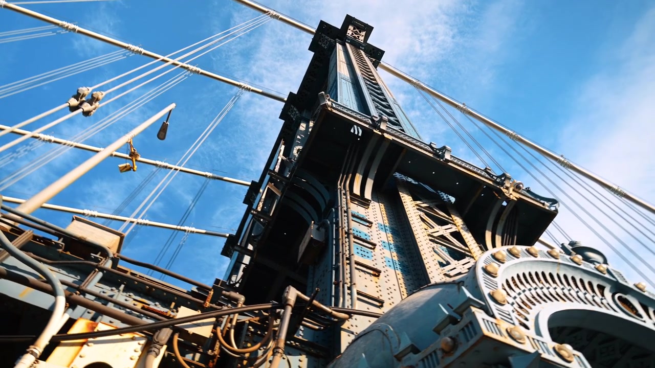 Torre e cavi di sospensione del Ponte di Manhattan visti dal basso. Travi in acciaio rivettate si ergono attraverso una rete di cavi contro un cielo azzurro brillante.