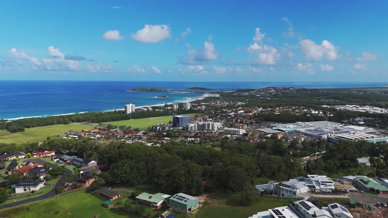 Aerial rising wide shot of Coffs Harbour Town during sunny day with blue sky. Australian coastline city with hoses and buildings in summer.