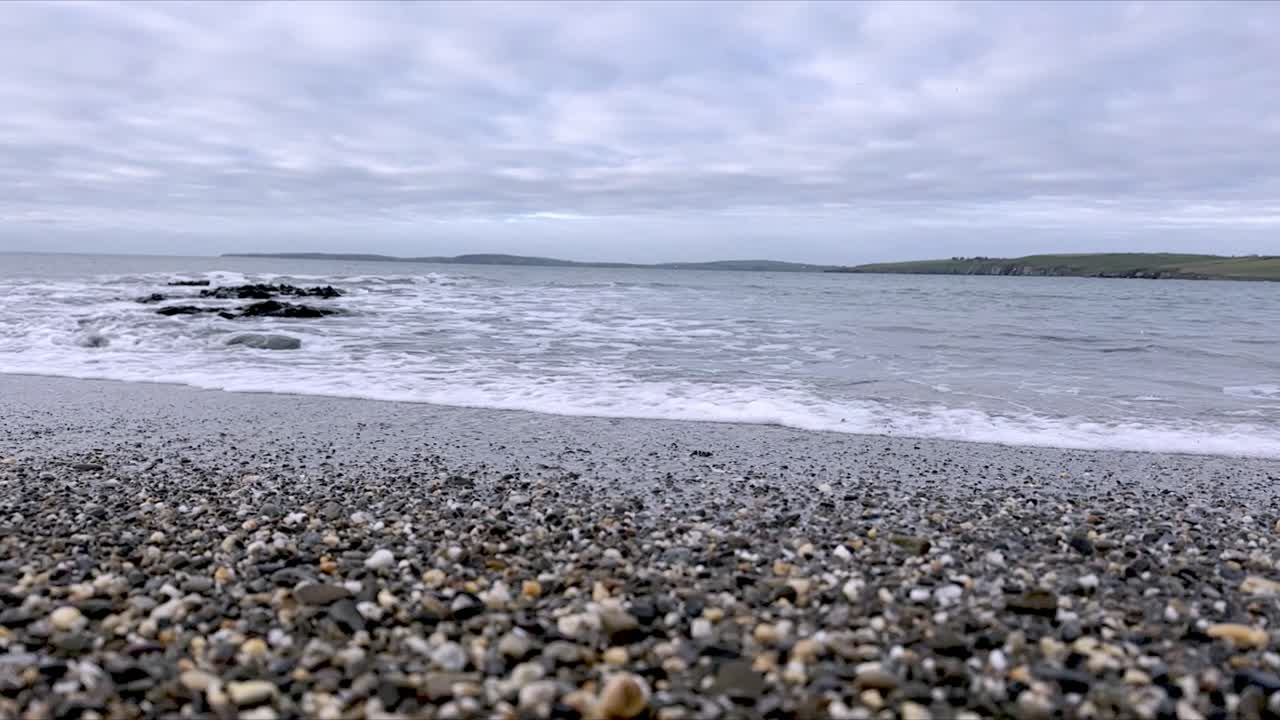 Småsten og sand med blide bølger, roen på en irsk strand