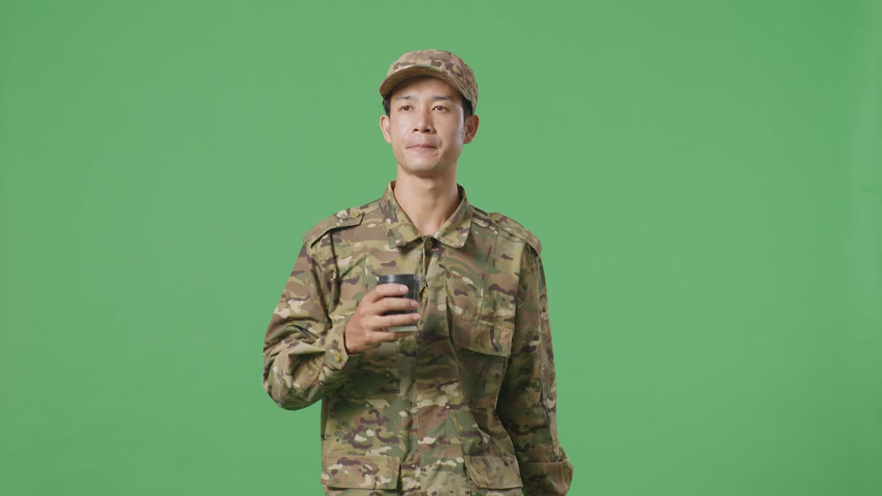 Uomo soldato asiatico che cammina e beve caffè nello studio con sfondo green screen