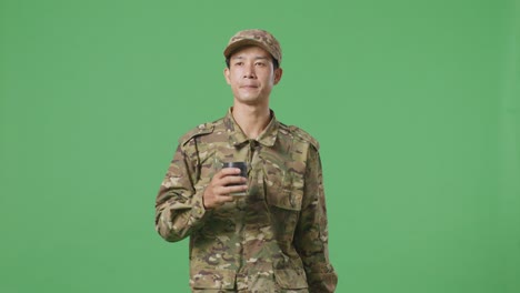 soldado asiático caminando y bebiendo café en el estudio de fondo de la pantalla verde