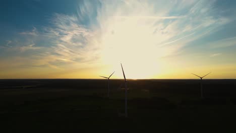 large wind turbines with blades in field aerial view bright orange sunset blue sky wind park slow motion drone turn