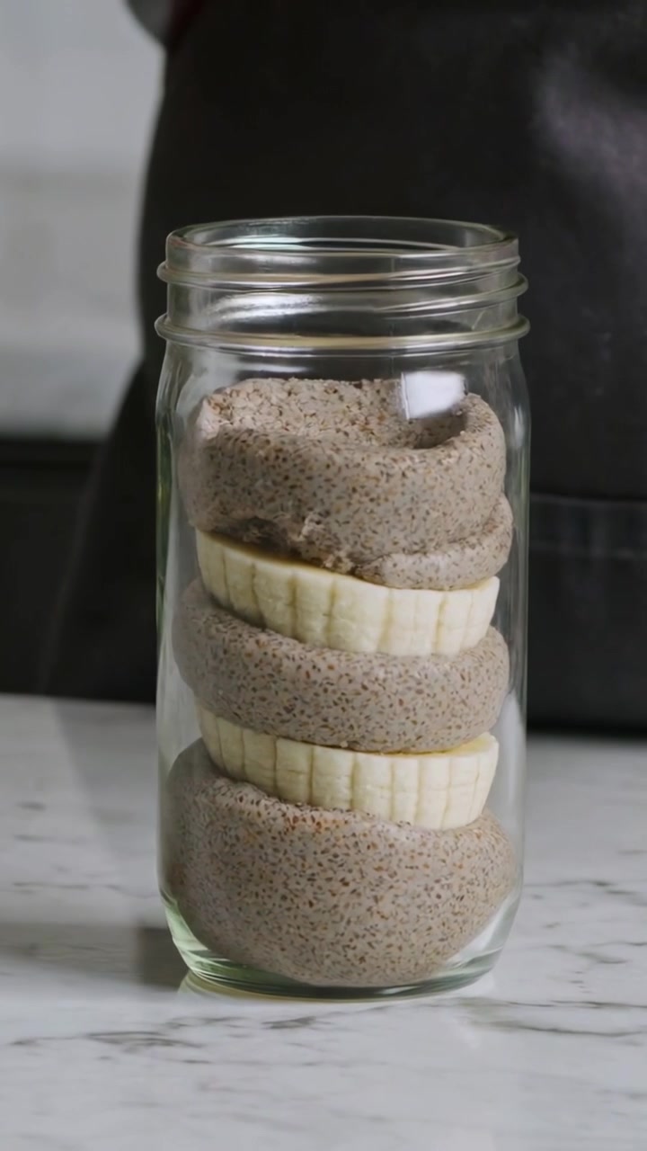 Video verticale: Cuoco in grembiule che, con un cucchiaio, completa le porzioni e le fette di banana in un barattolo di vetro su marmo.