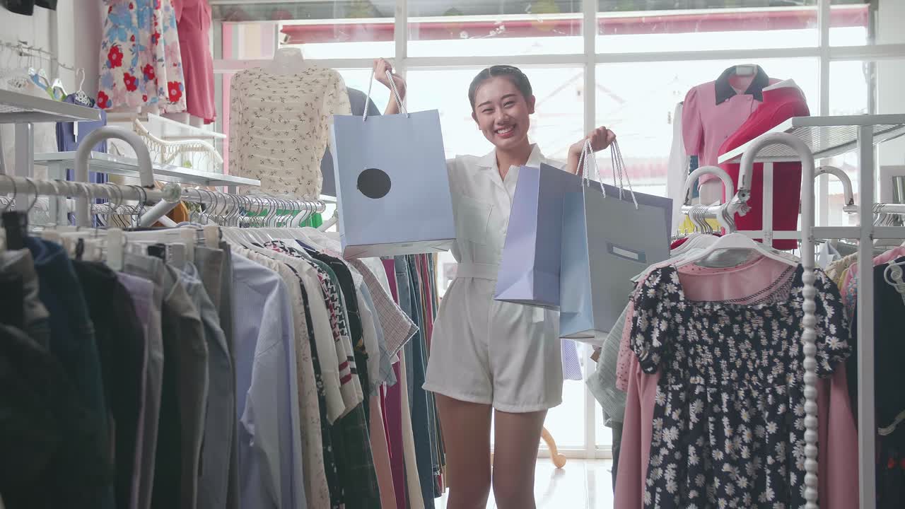 부티크에서 쇼핑하는 동안 카메라에 미소 짓는 쇼핑 가방을 가진 젊은 아시아 여성