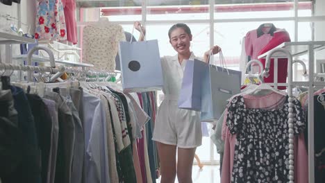 joven asiática con las bolsas de compras sonriendo a la cámara mientras compra en la boutique