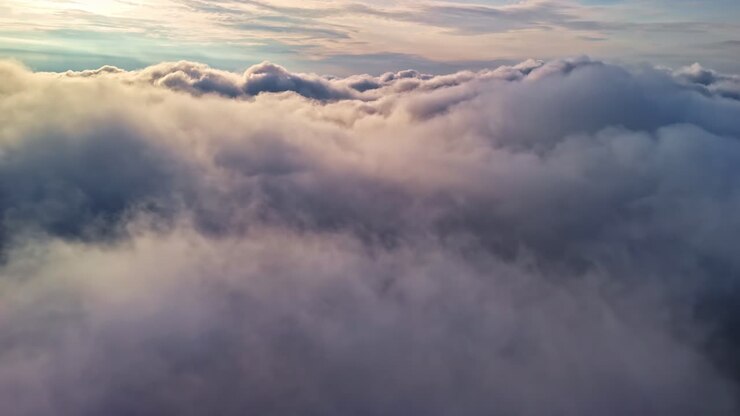Aerial drone shot skimming above a dense cloud layer under a soft, diffuse grey sky. No horizon, no ground — only clouds filling the frame in all directions