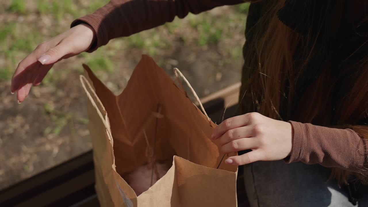 Coloca suavemente sus pertenencias; la mujer arregla sus objetos con delicadeza y elegancia sobre un banco, y posiciona con gracia y aplomo su bolso y sus pertenencias sobre el banco.