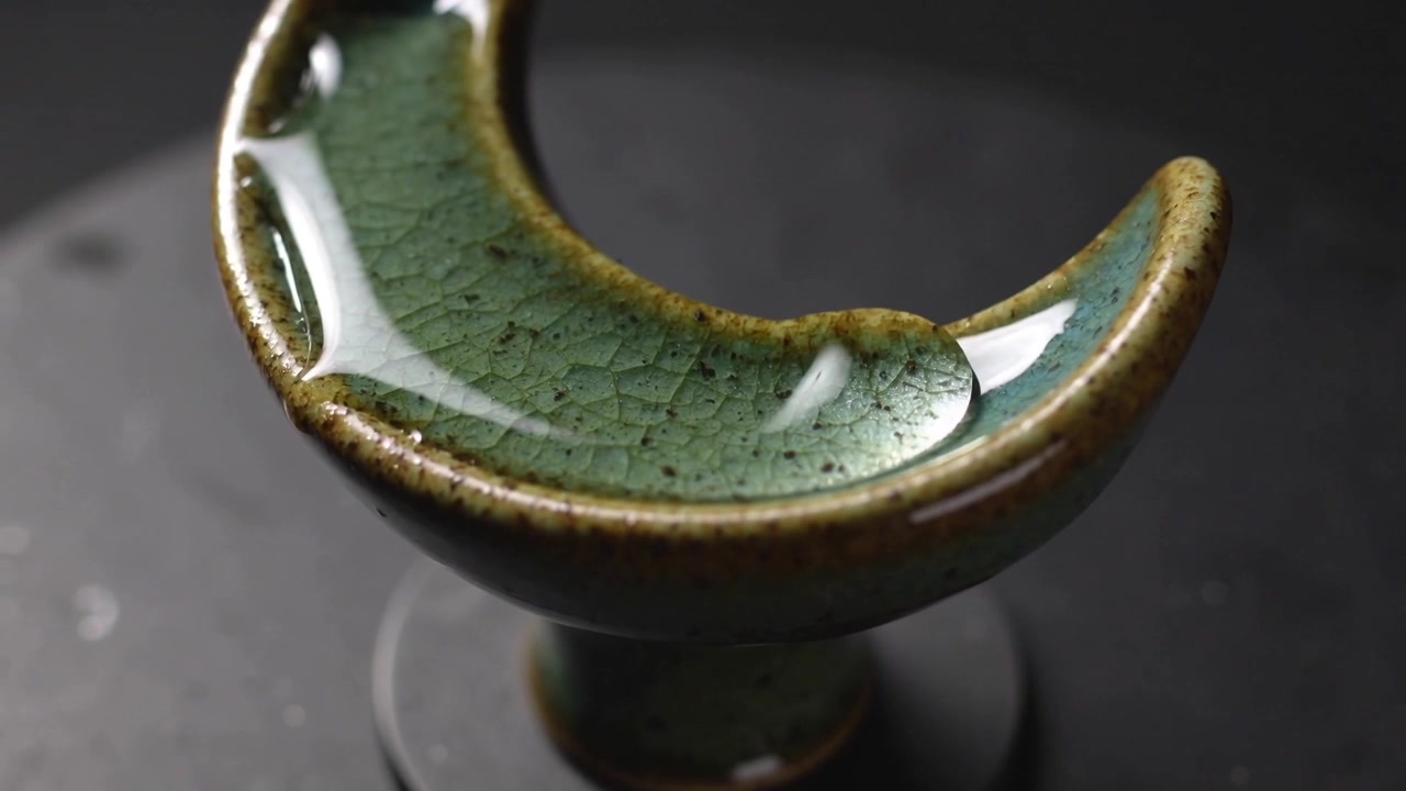 Shifting green crescent bowl wobbling on black base, moving water rightward from platform spin