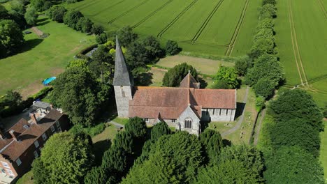 Aerial-upward-tilt-shot-of-St-John-the-Evangelist-church-in-Ickham,-Kent,-with-a-few-village-houses-in-the-background