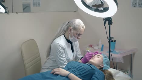 beautician with long white hair applies permanent make-up