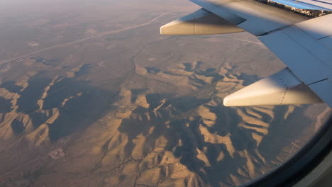 volando sobre las montañas, vista aérea de las cimas de las montañas y el ala del avión desde la ventana -- 4k