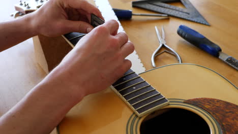 hands of a luthier craftsman measuring and leveling an acoustic guitar neck fretboard on a wood workshop bench with lutherie tools